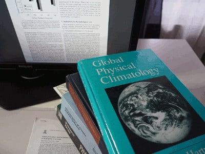 Books on physical climatology and dynamic meteorology, stacked in front of a computer screen